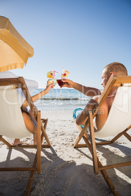 Couple clinking their glasses while relaxing on their deck chair