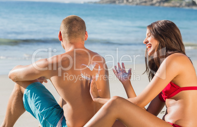 Cheerful attractive woman applying sun cream on her boyfriends b