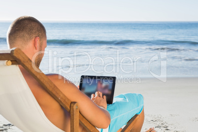 Handsome man scrolling on his tablet pc while sunbathing