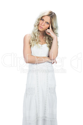 Frowning attractive model in white dress posing touching her hea