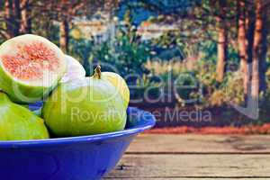 Bowl of fresh figs on rustic wooden table against forest backgro