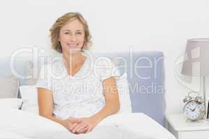 Blonde woman sitting in bed smiling at camera