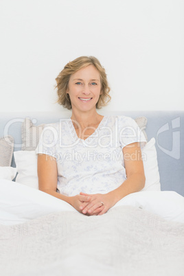 Blonde happy woman sitting in bed smiling at camera