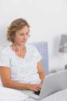 Blonde woman sitting in bed using laptop