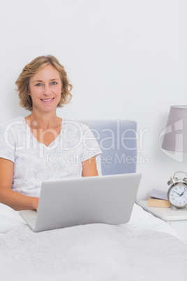 Smiling blonde woman sitting in bed using laptop