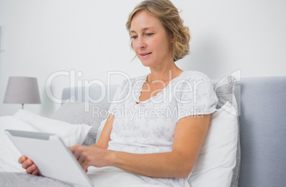 Blonde smiling woman sitting in bed using tablet pc