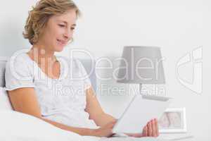 Content blonde woman sitting in bed using tablet pc