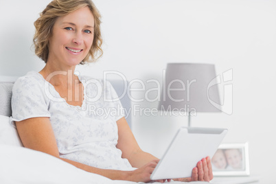 Cheerful blonde woman sitting in bed using tablet pc