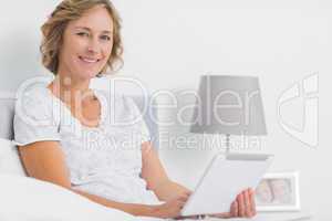 Cheerful blonde woman sitting in bed using tablet pc