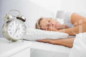 Blonde woman asleep in bed while her alarm shows the early time