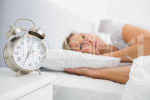 Blonde woman lying in bed while her alarm shows the early time