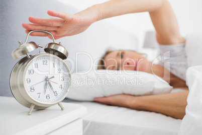 Tired blonde woman turning off her alarm in the morning