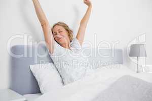 Blonde woman stretching and smiling in bed in the morning