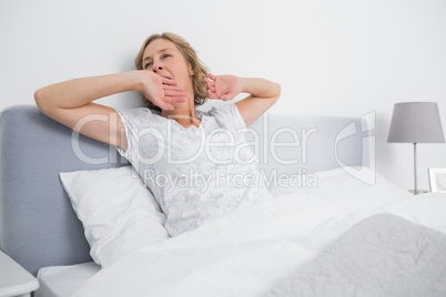 Blonde woman yawning and stretching in bed in the morning