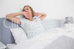 Blonde woman yawning and stretching in bed in the morning
