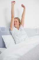 Well rested blonde woman stretching in bed