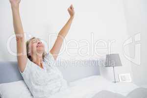 Well rested blonde woman stretching in bed and smiling