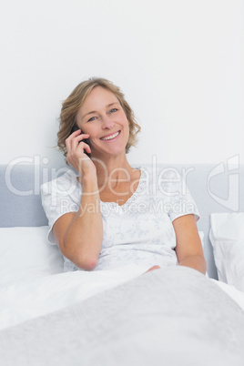 Happy blonde woman on the phone in bed smiling at camera Happy blonde woman on the phone in bed smiling at camera