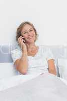 Happy blonde woman on the phone in bed smiling at camera