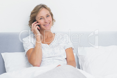 Blonde woman on the phone in bed smiling at camera