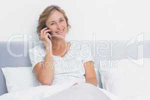 Blonde woman on the phone in bed smiling at camera