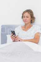 Blonde woman sending text message in bed