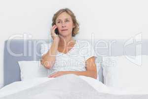 Serious blonde woman making phone call in bed