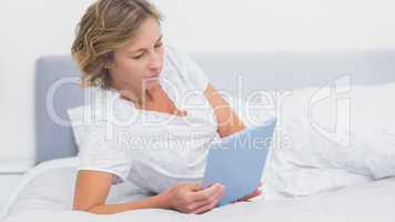 Happy blonde woman lying on bed using tablet pc