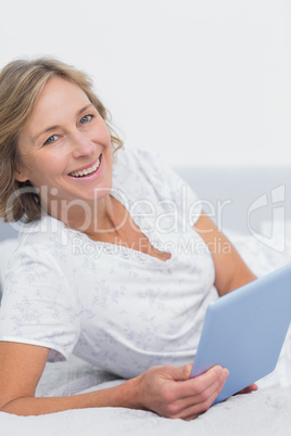 Smiling blonde woman lying on bed using tablet pc