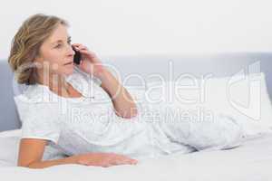Serious blonde woman lying on bed making a phone call