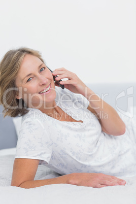 Smiling blonde woman lying on bed making a phone call