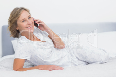 Happy blonde woman lying on bed making a phone call