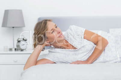 Thoughtful blonde woman lying on bed