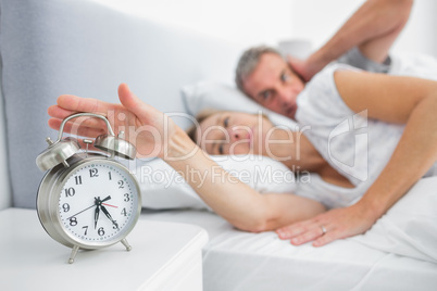 Wife turning off alarm clock as husband is covering ears