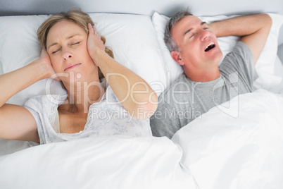 Wife blocking her ears from noise of husband snoring