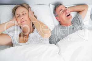 Wife blocking her ears from noise of husband snoring