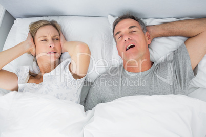 Annoyed wife blocking her ears from noise of husband snoring