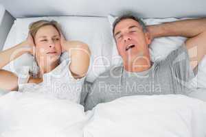 Annoyed wife blocking her ears from noise of husband snoring