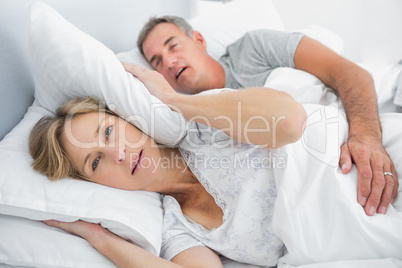 Irritated wife blocking her ears from noise of husband snoring