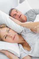 Tired wife blocking her ears from noise of husband snoring looki