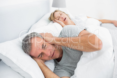 Tired man blocking his ears from noise of wife snoring