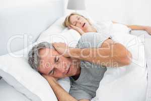 Tired man blocking his ears from noise of wife snoring