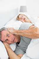 Irritated man blocking his ears from noise of wife snoring