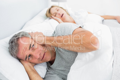 Fed up man blocking his ears from noise of wife snoring