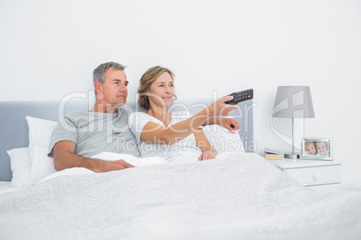 Happy couple watching tv in bed