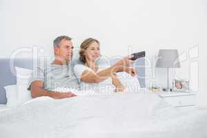 Happy couple watching tv in bed