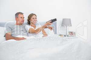 Cheerful couple watching tv in bed