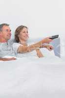 Relaxed couple watching tv in bed