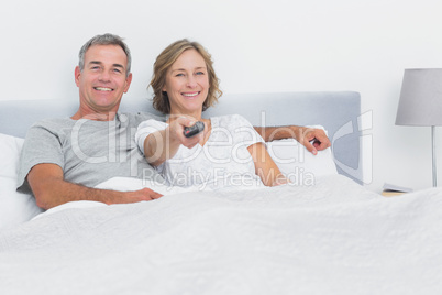 Relaxed couple watching tv in bed looking at camera