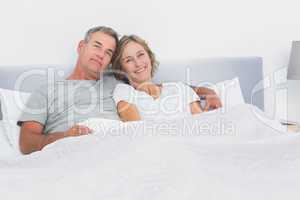 Relaxed couple cuddling in bed looking at camera